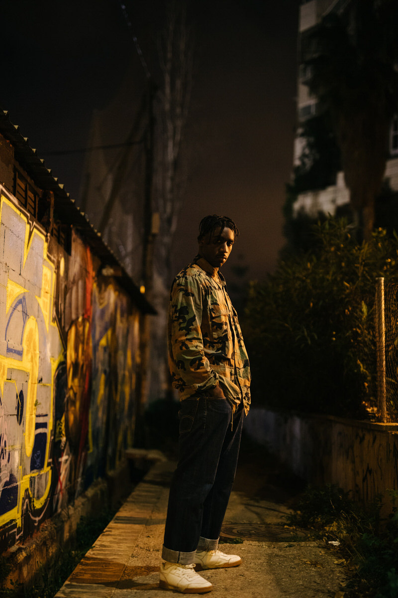 Black man standing near graffiti wall at night