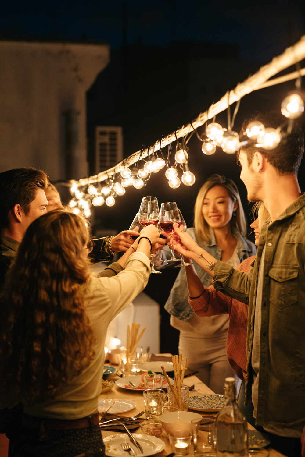 Friends clinking glasses under light garland