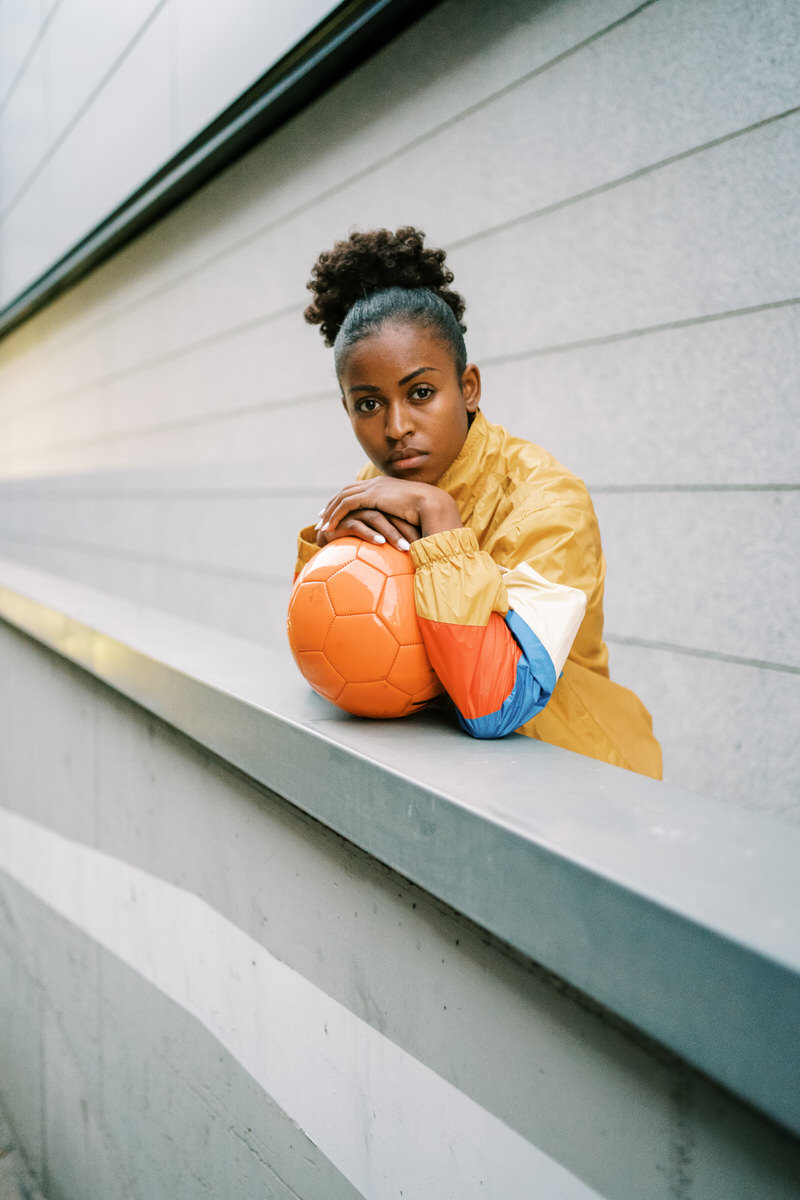 Serious female footballer standing with ball in street